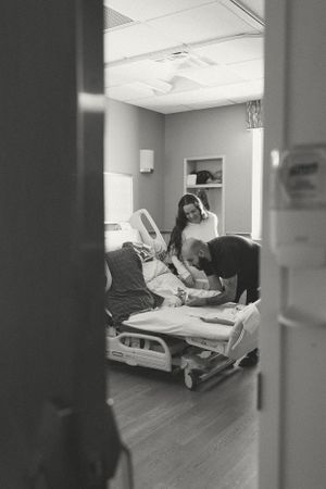 Black and white photo through doorway showing medical staff caring for patient in hospital room bed.
