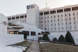 Large medical facility building with modern entrance canopy and white exterior walls during winter weather.