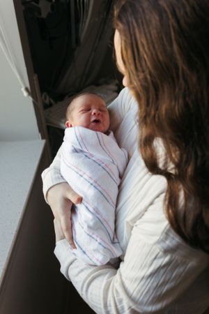 A swaddled newborn baby smiles while being held in a cozy interior with natural window light.