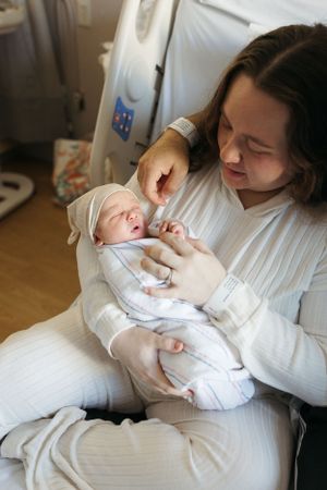 A person in white clothing cradles and tends to a tiny newborn baby wrapped in soft white clothing.