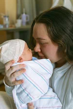 Tender moment between parent and newborn baby wrapped in striped blanket in hospital setting.