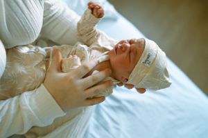 A newborn baby wrapped in a hospital blanket is being gently held by medical staff during a checkup.