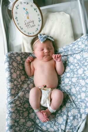 Three sleeping newborn babies lie on blue floral fabric with embroidered name hoops displayed above them.