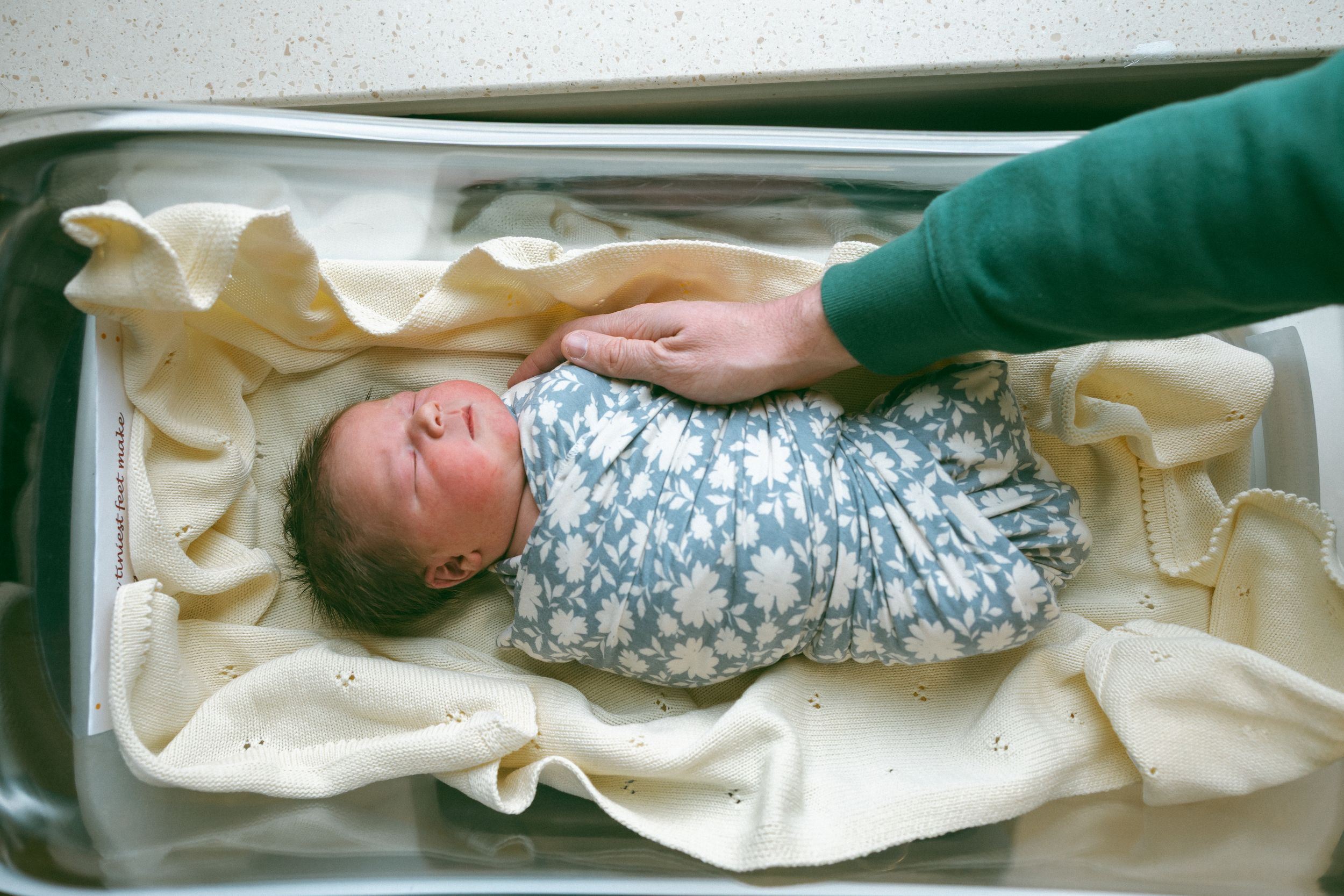 A row of newborn babies sleeping in hospital bassinets wrapped in blankets and swaddling.