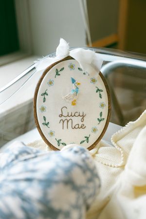 Delicate name tags with floral designs and cursive text 'Lucy Mae' displayed on soft white fabric in natural light.