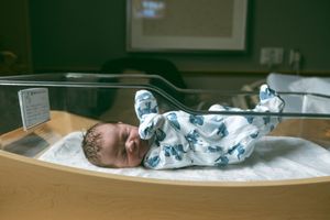 Newborn baby rests peacefully in hospital bassinet wearing blue and white patterned sleepwear.
