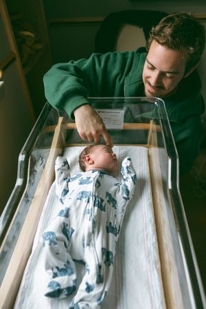 A newborn baby sleeps peacefully in a hospital bassinet while being watched over in a green room.