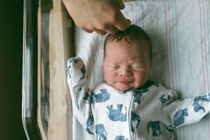 A sleeping baby wearing a white and blue patterned onesie rests peacefully in a crib.