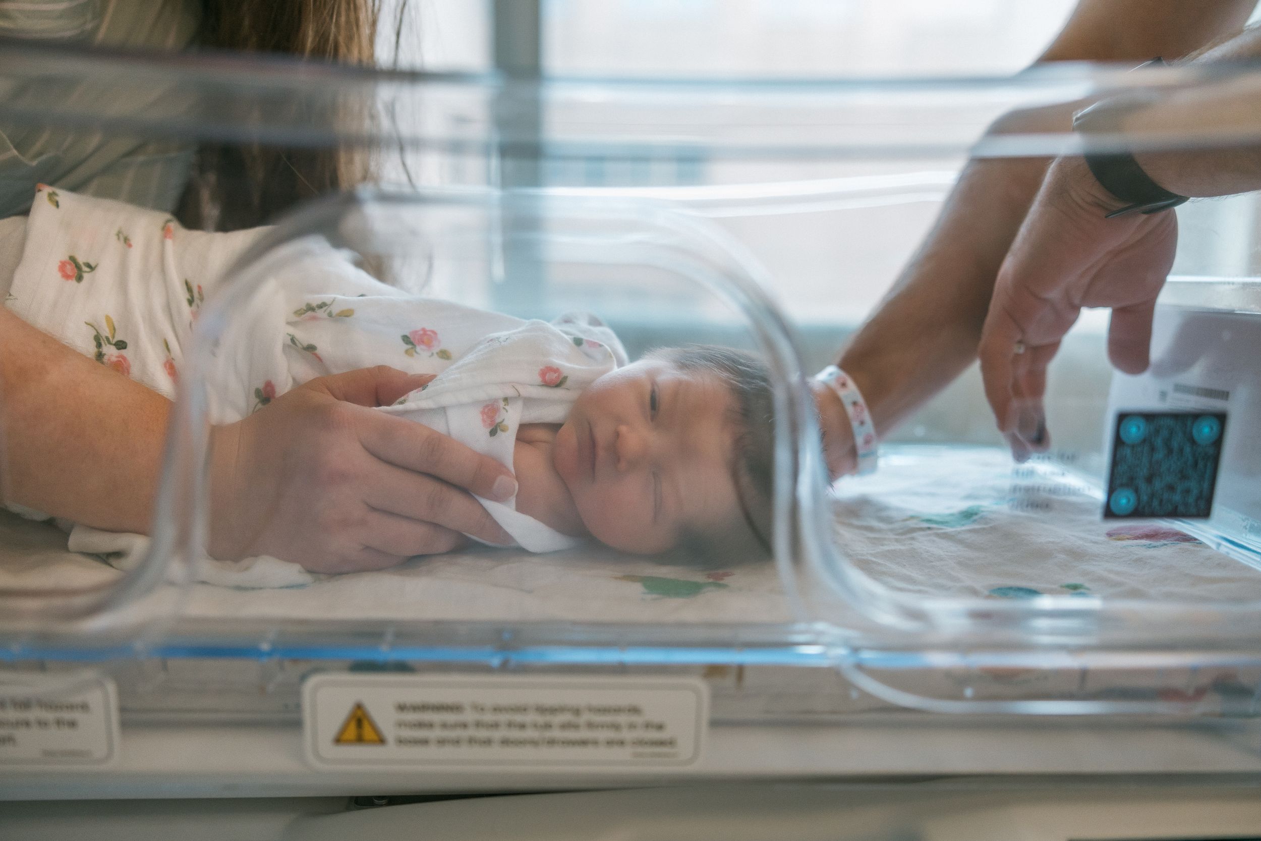 Premature newborn baby resting in a hospital incubator with medical monitoring equipment nearby.