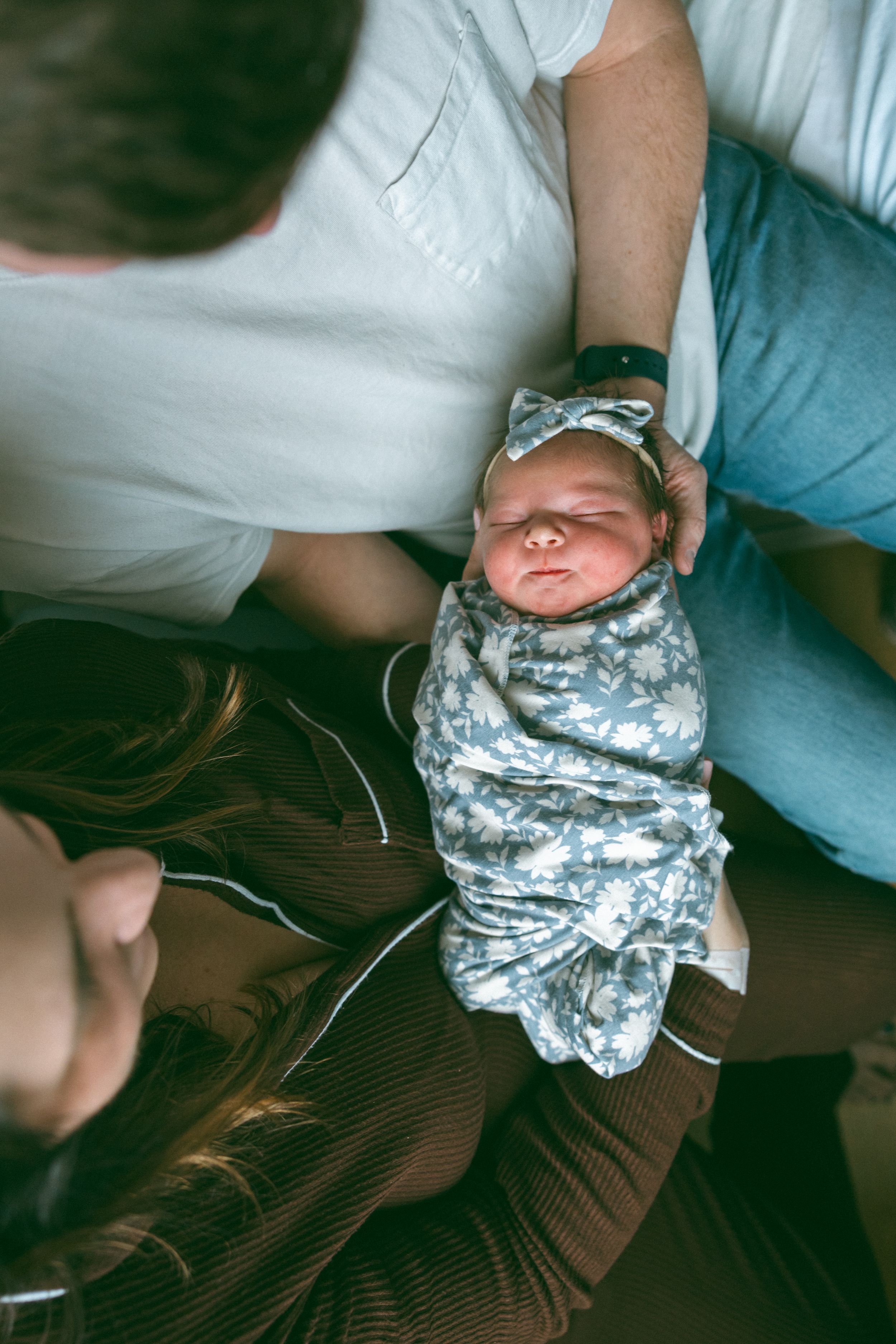 A baby wrapped in a floral print blanket is being held while laying on a brown surface.