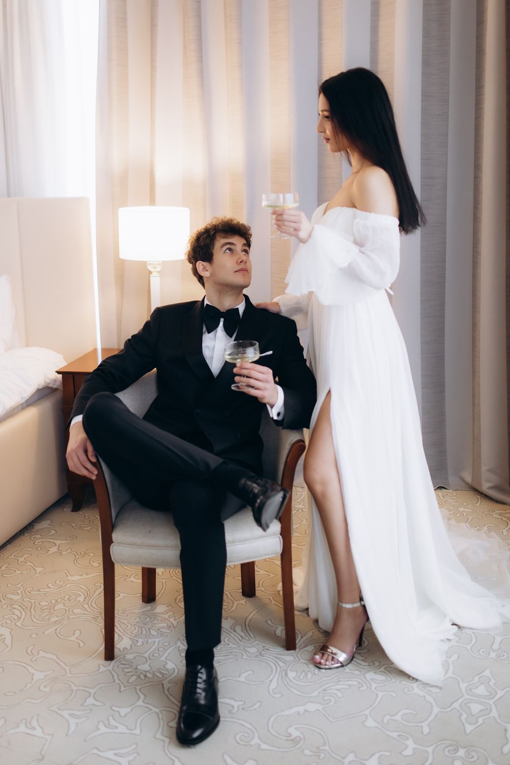 Formal couple sharing drinks in an elegant room with white curtains and modern decor.