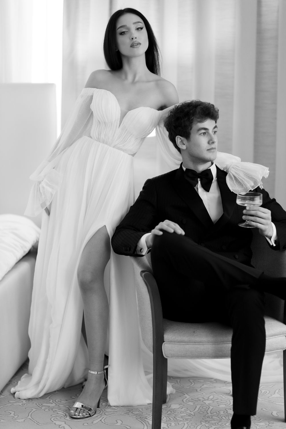 Elegant black and white photo of a couple in formal wear, with a woman in white gown and man in tuxedo posing in studio.