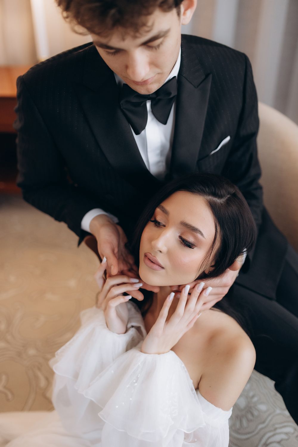 A tender romantic moment between a couple in formal attire with a black tuxedo and white off-shoulder dress.