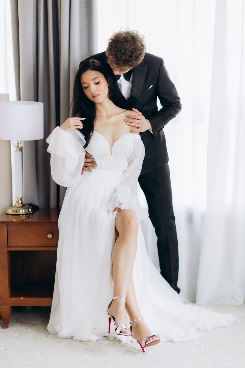 A romantic bridal portrait featuring a couple in a white gown and black tuxedo sharing an intimate moment by a window.