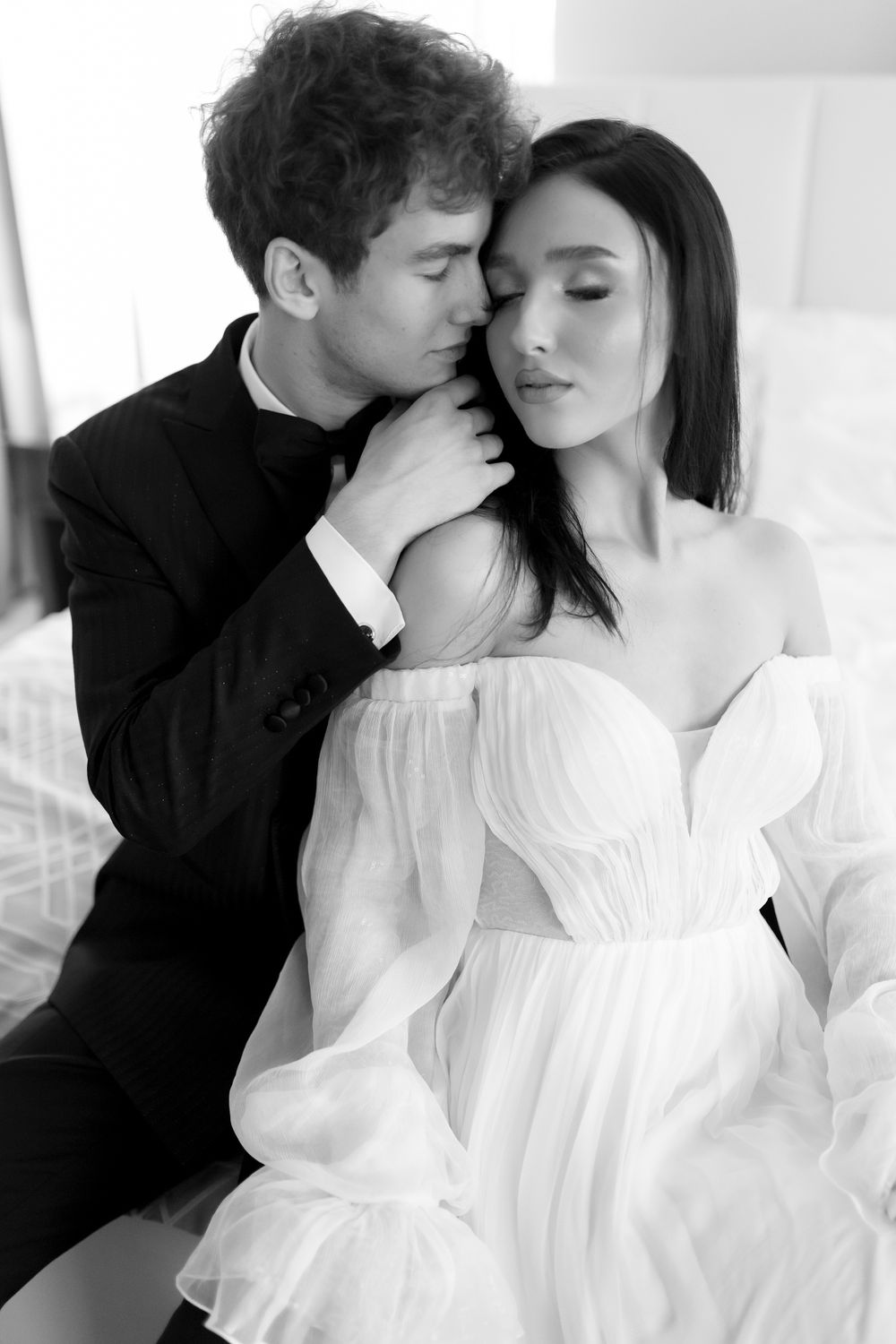 A romantic black and white portrait of a couple in formal attire with him in black and her in a flowing white dress.