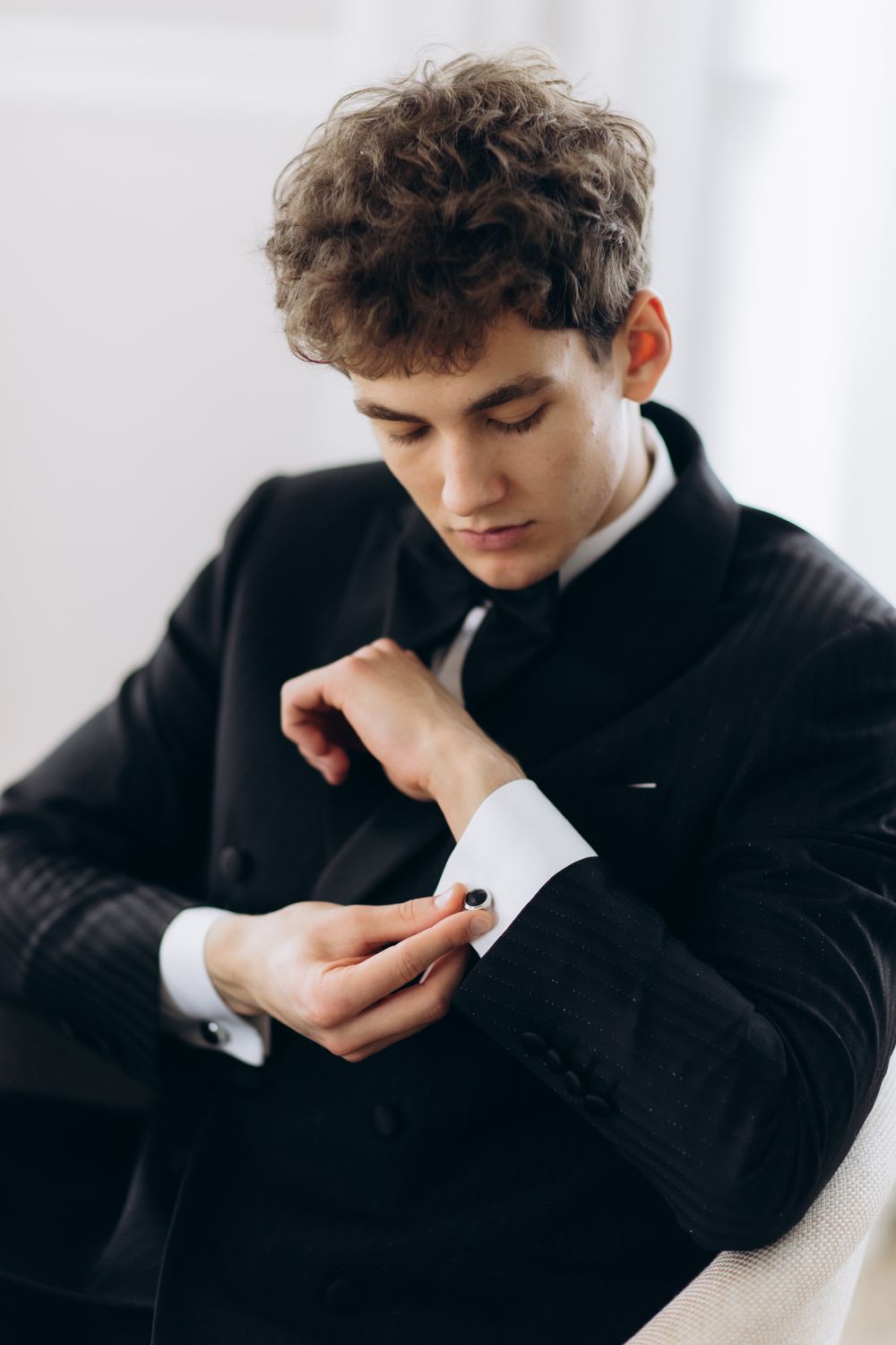 Someone wearing a black suit adjusts their cufflink while getting dressed in formal attire.