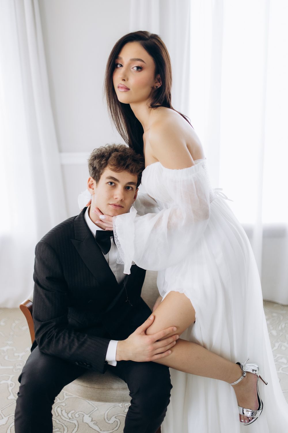 A romantic wedding photo featuring a couple in black and white attire posing intimately against a light backdrop.