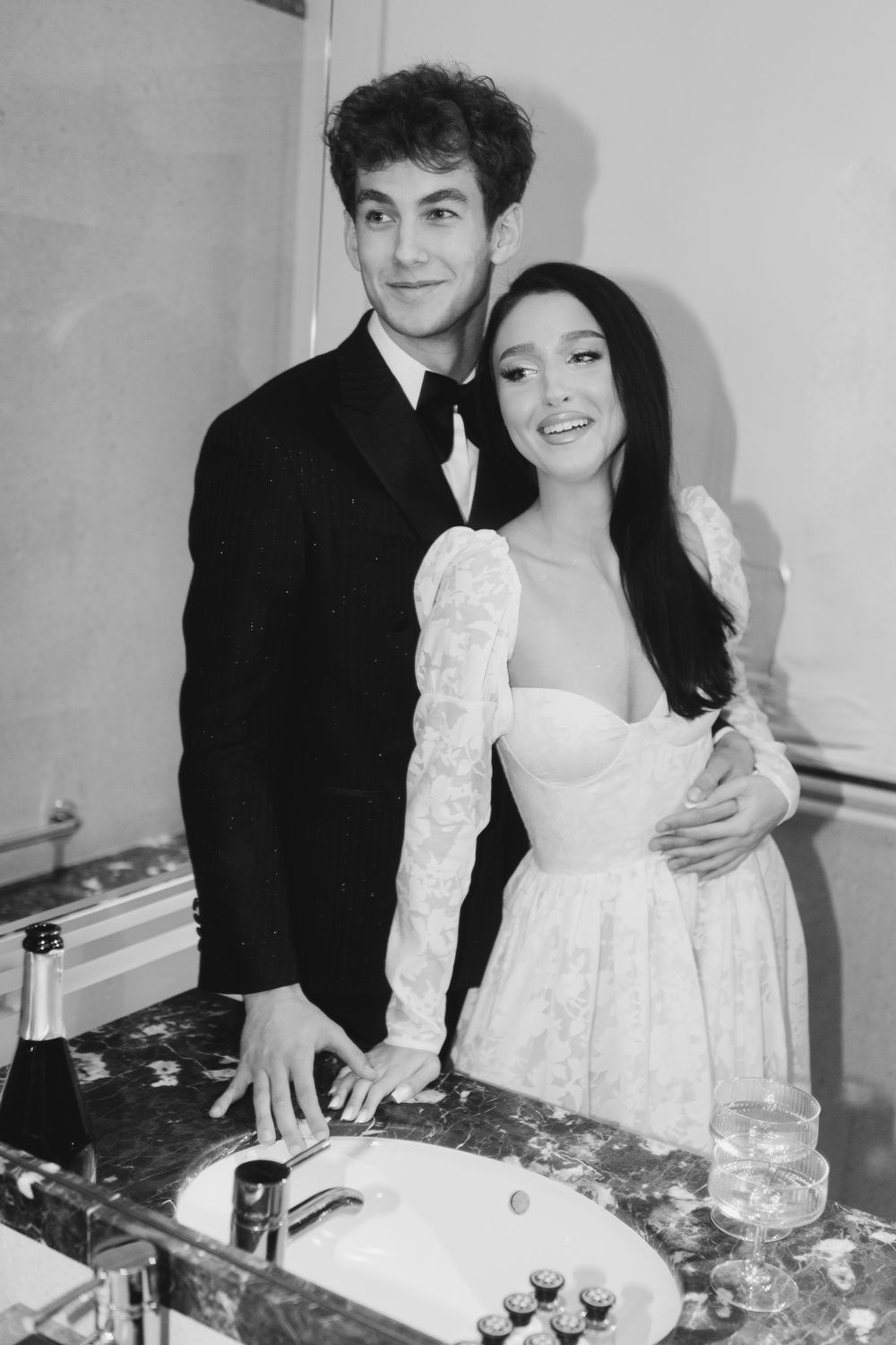 A black and white photo of a couple cutting their wedding cake, with the bride wearing a white lace dress.