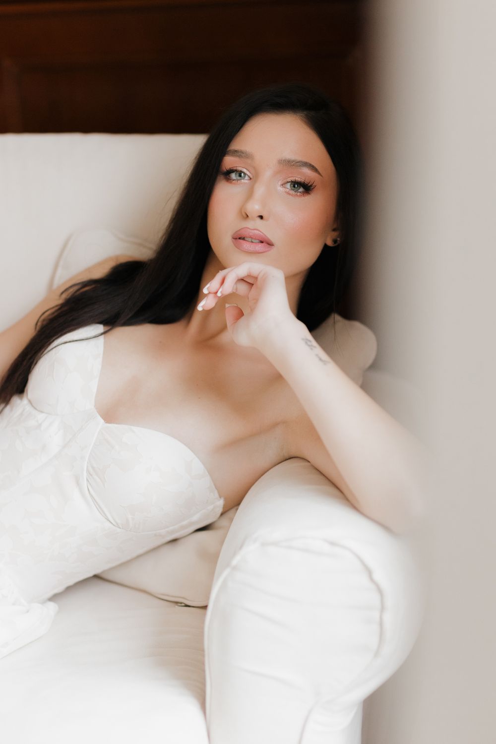 Elegant fashion portrait of a woman in a white strapless dress lounging on a light-colored couch.