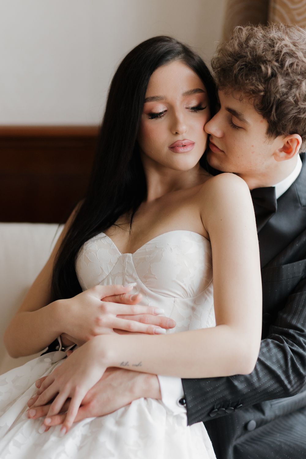 A tender embrace between newlyweds, with the bride in a white corset dress and groom in black suit sharing an intimate moment.