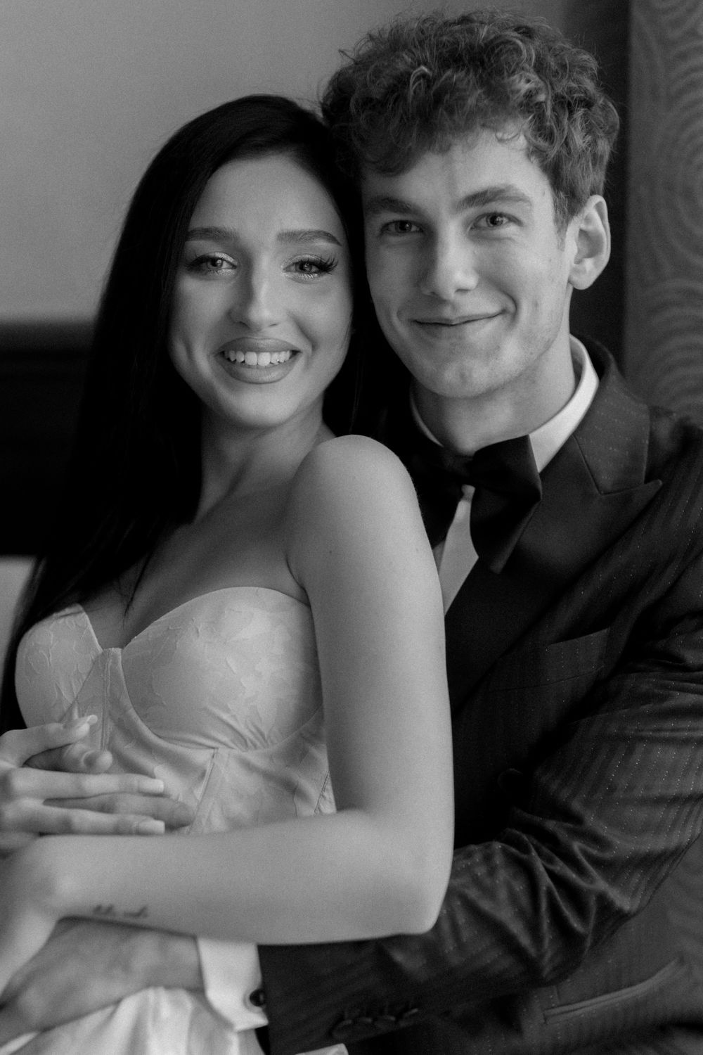 A glamorous black and white portrait of a couple in formal attire smiling warmly at the camera.