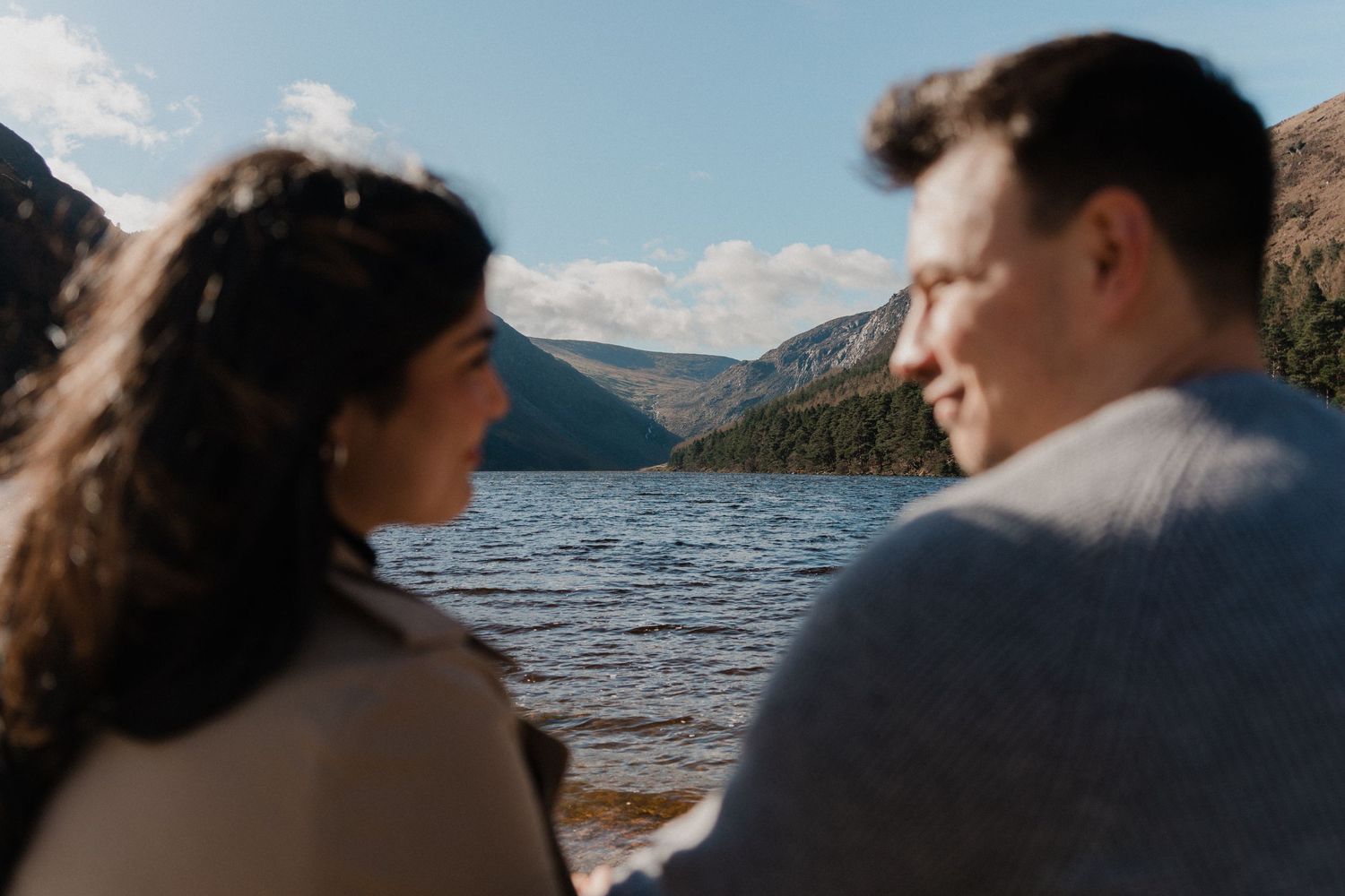 A couple embraces against the backdrop of a serene mountain lake and cloudy sky.