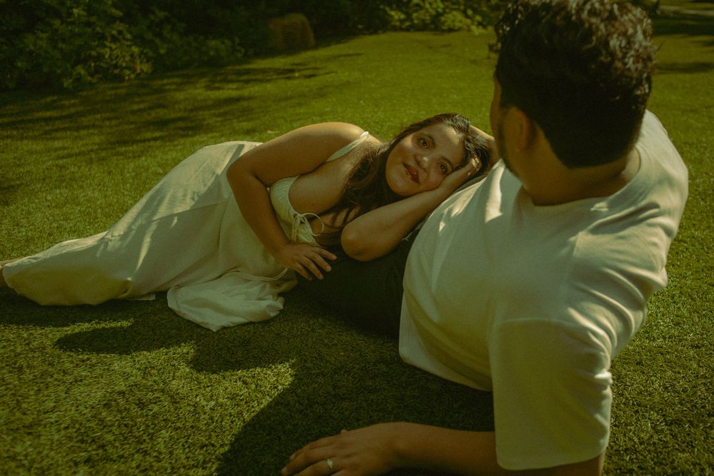 Two people lounging together on green grass during a sunny summer day, with a warm, vintage-style filter effect.