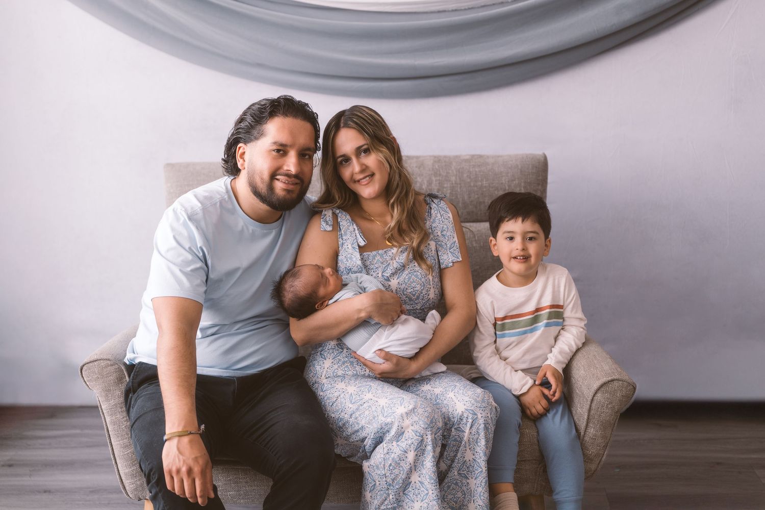 Family relaxing together on gray couch in living room setting.