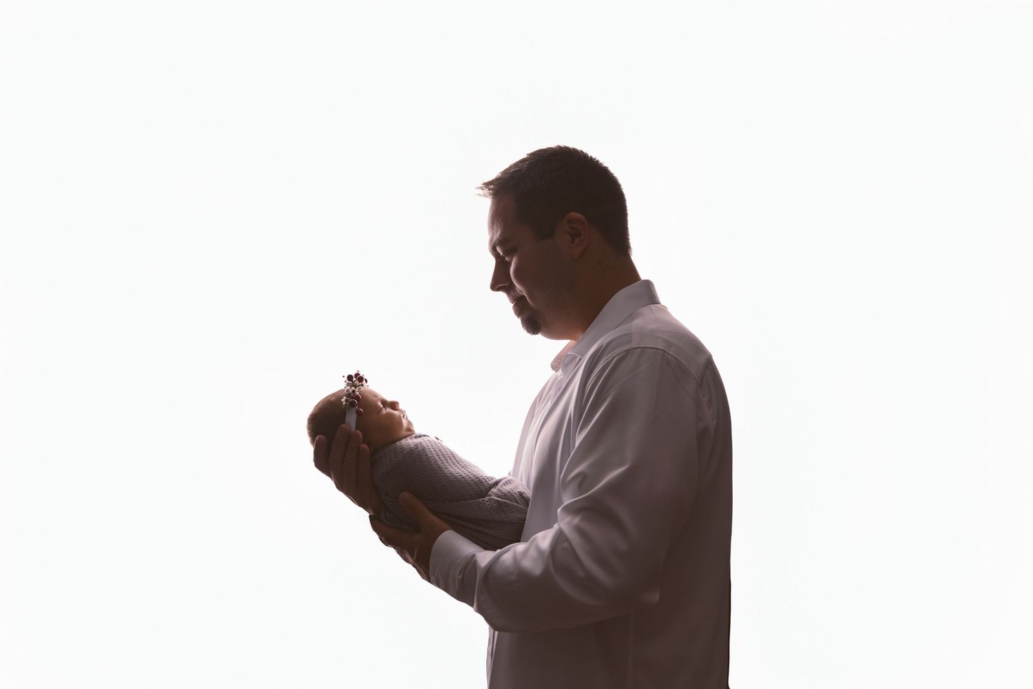 Person in gray shirt holding sleeping newborn against white background.