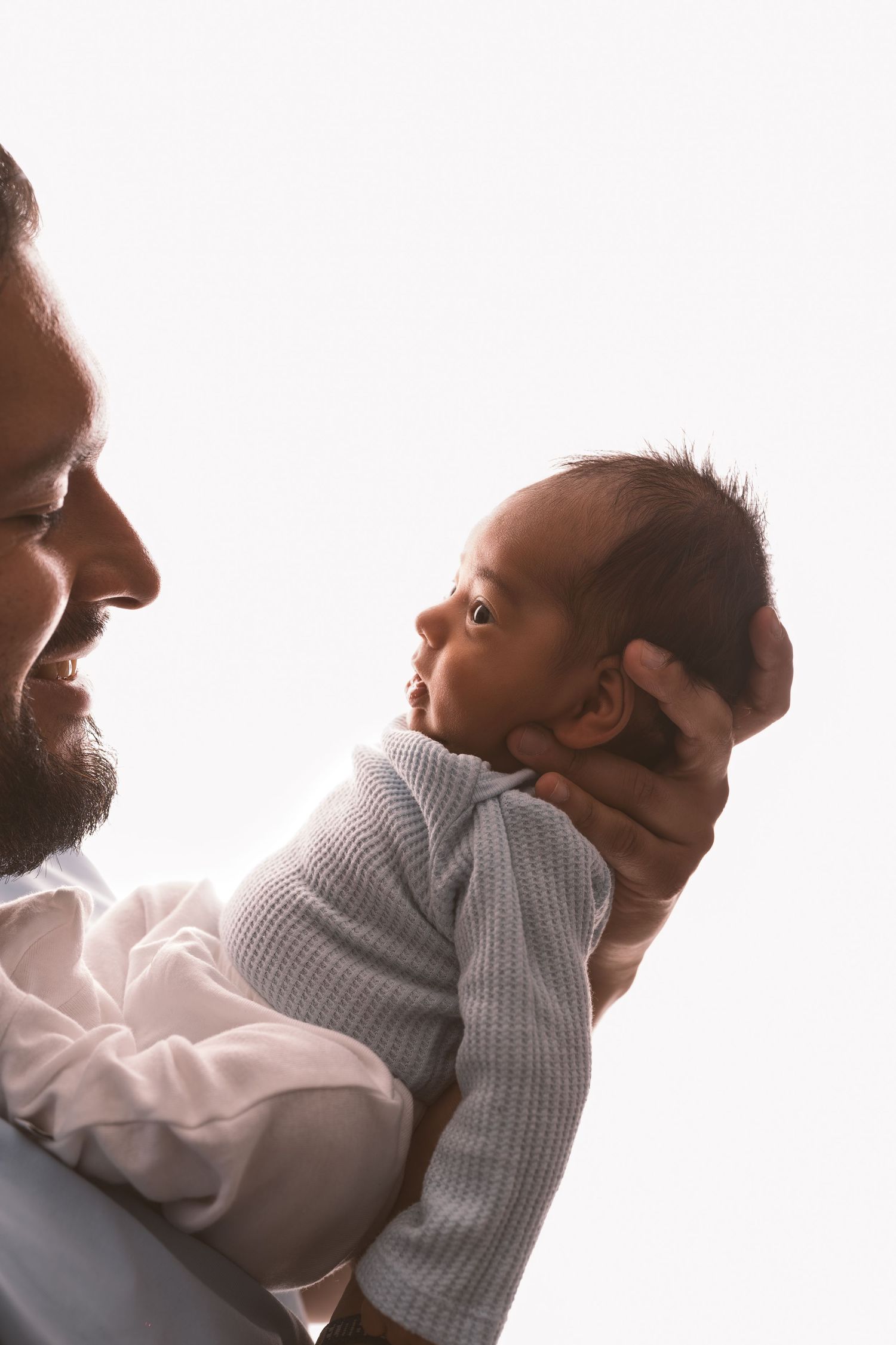 A tender moment captured in soft light showing a parent holding and kissing a newborn baby.