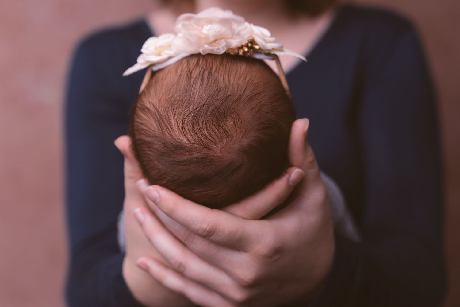 Hands gently cradling sleeping newborn wrapped in soft fabric.