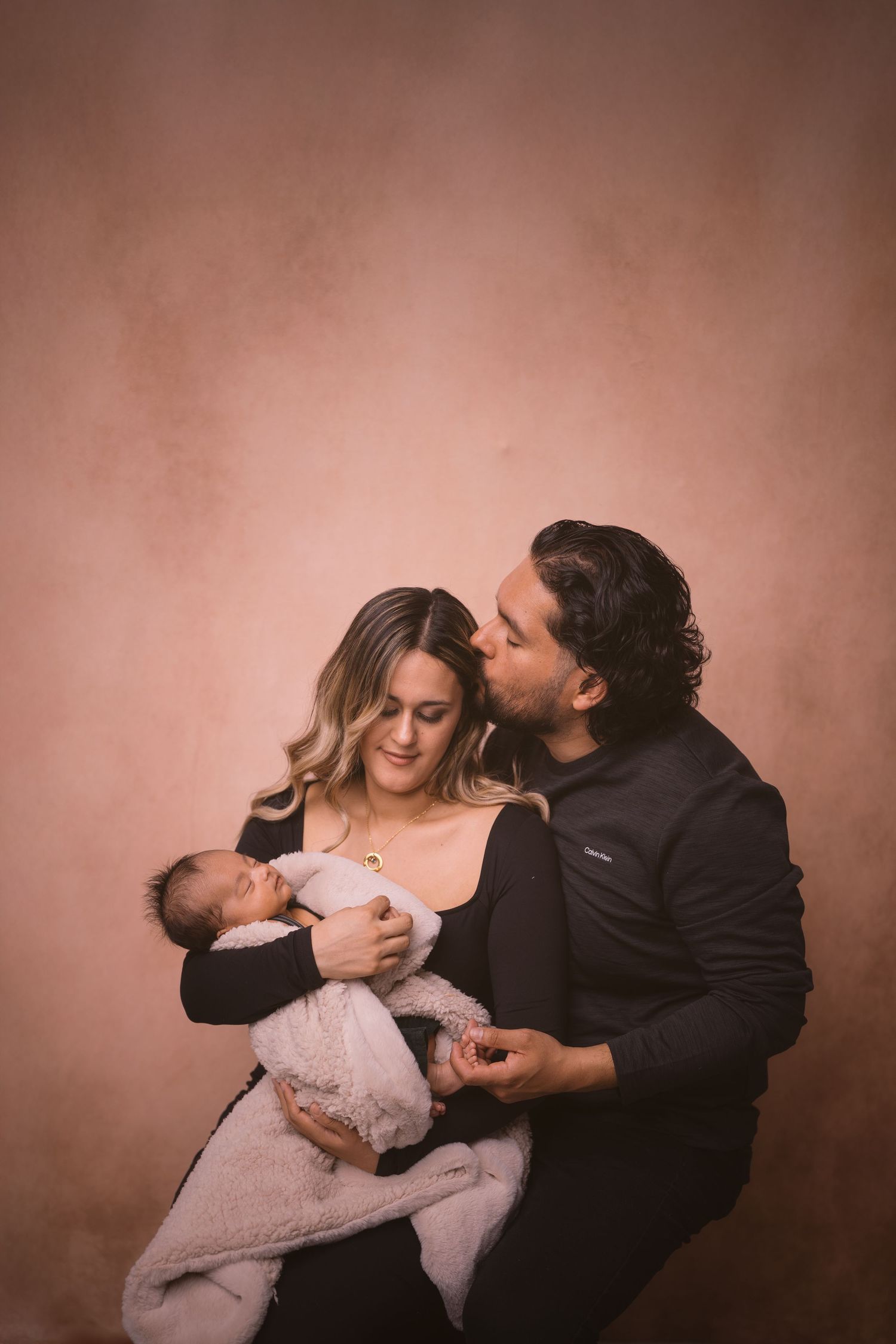 Intimate family portrait session showing loving interactions between parents and child on brown backdrop.