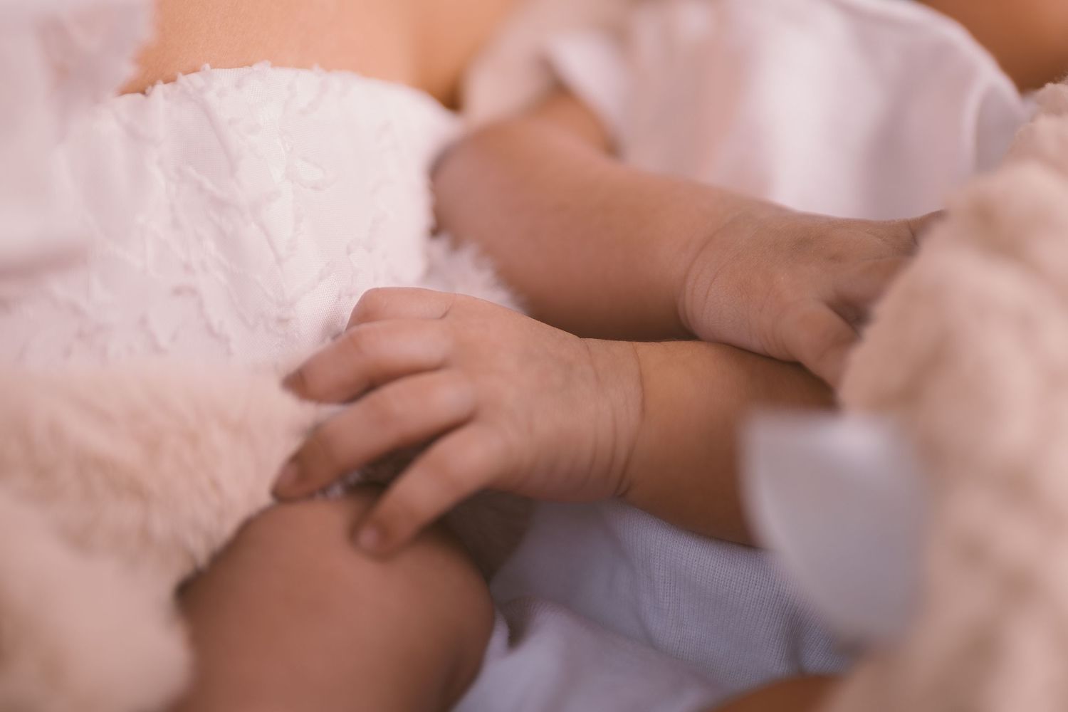 Gentle close-up of small baby hands against soft white fabric.