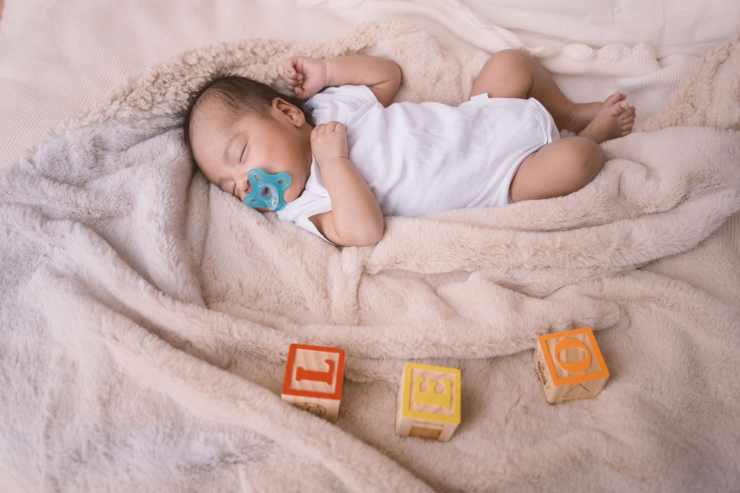 Newborn baby sleeping peacefully on white blanket with colorful alphabet blocks.