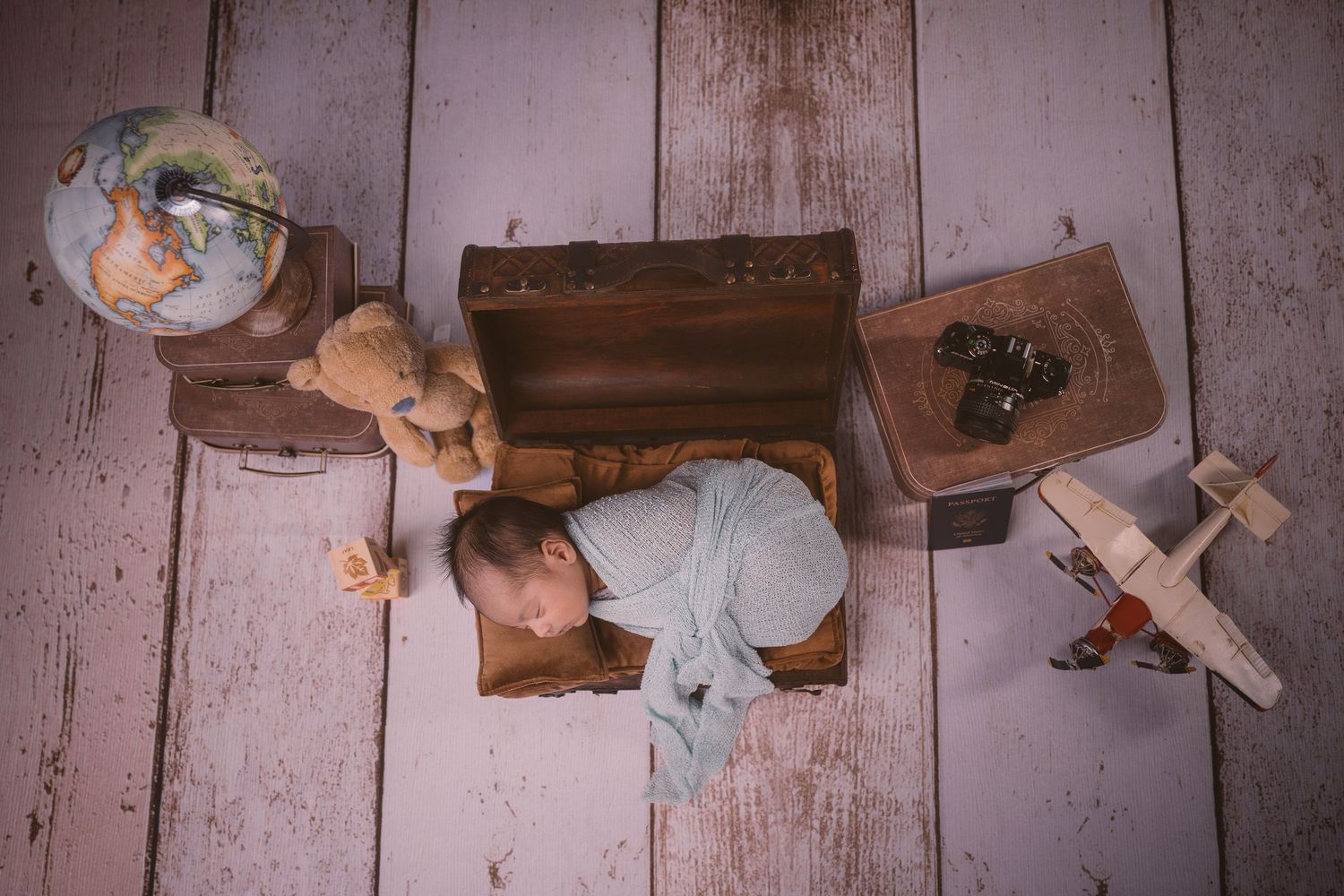 Creative newborn photography setup with vintage travel theme including wooden props and airplane toys.