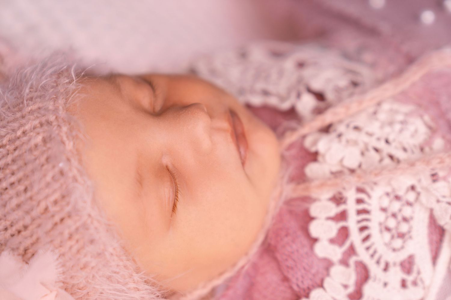 Sleeping newborn on pink textured fabric with delicate lace details.