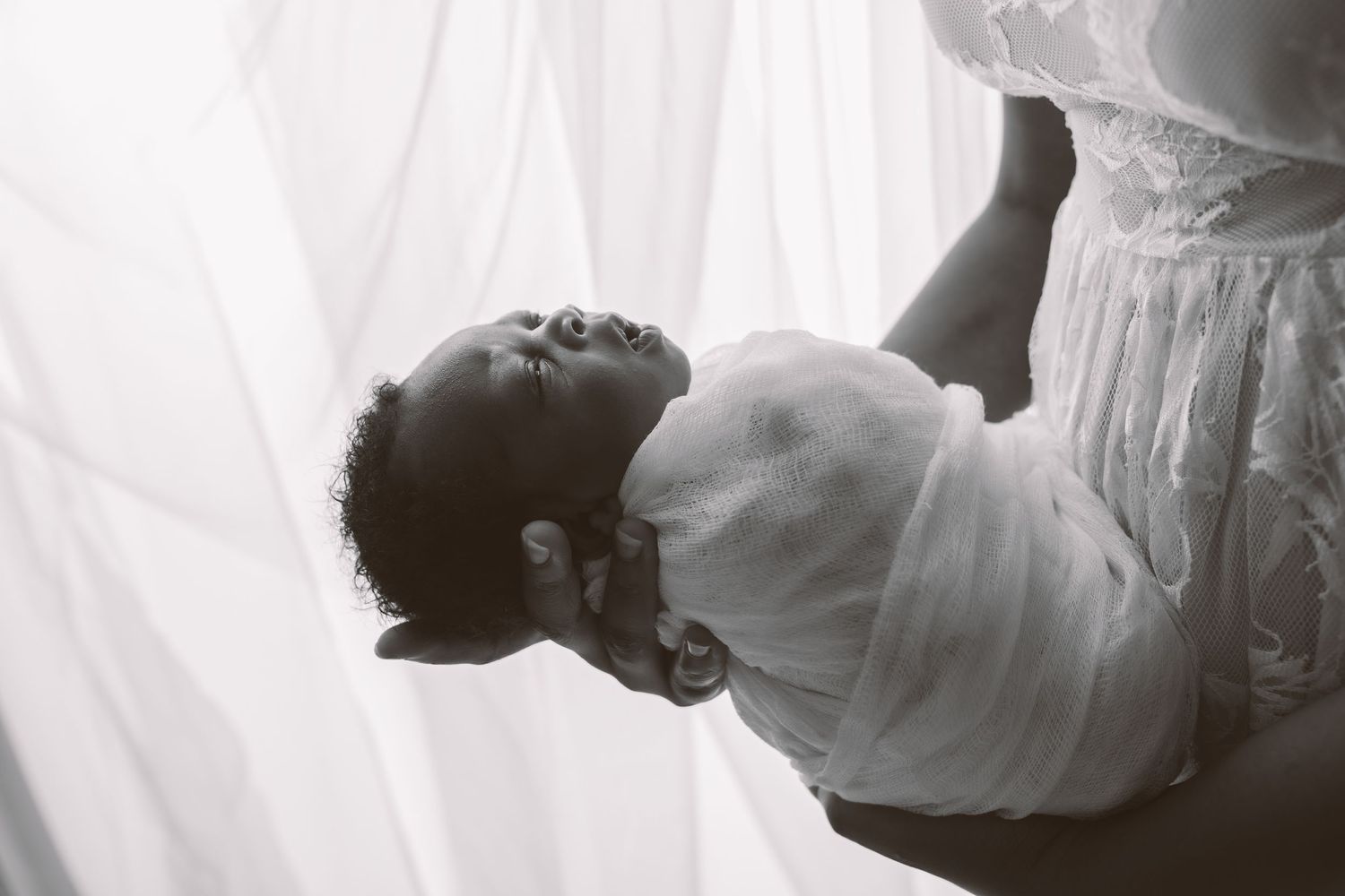 Artistic black and white portrait of baby wrapped in flowing white fabric.