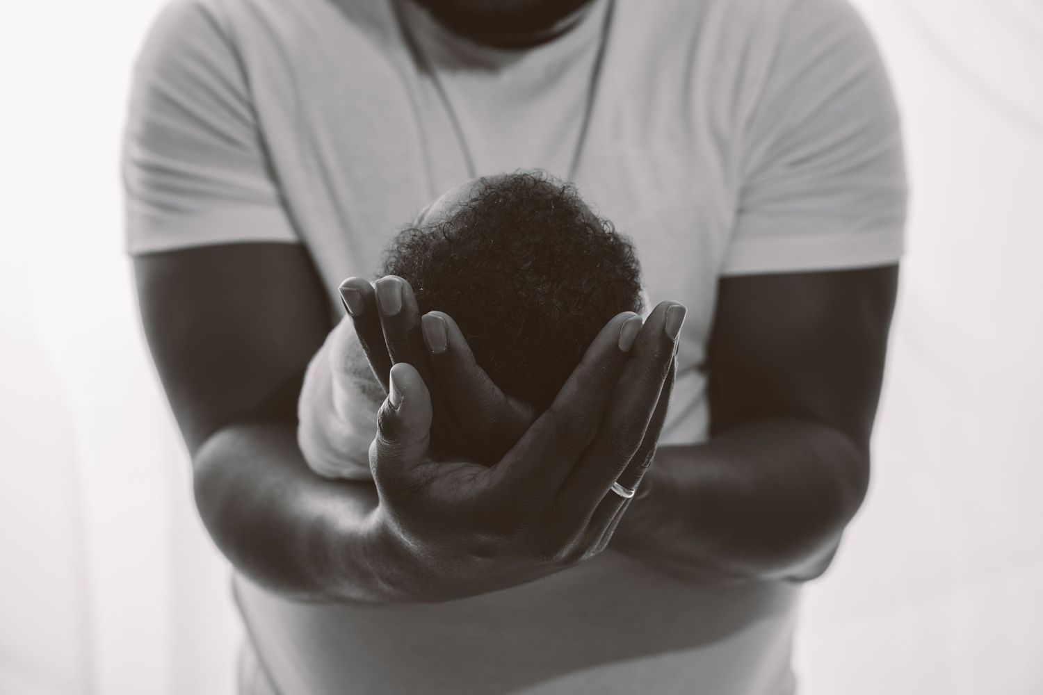 Intimate black and white maternity photoshoot showing a couple embracing against a white backdrop.