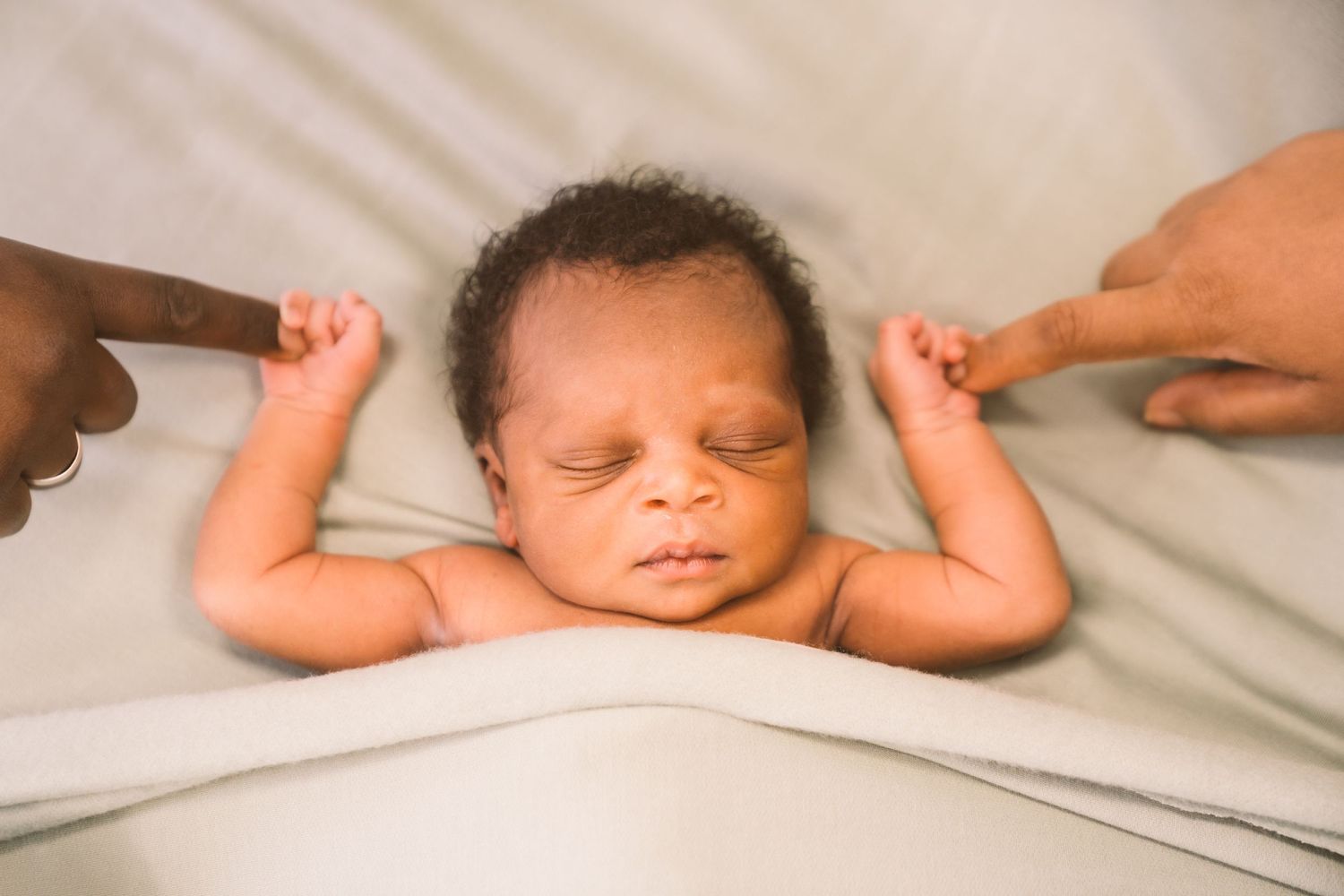Sleeping baby with arms outstretched on white bedding.
