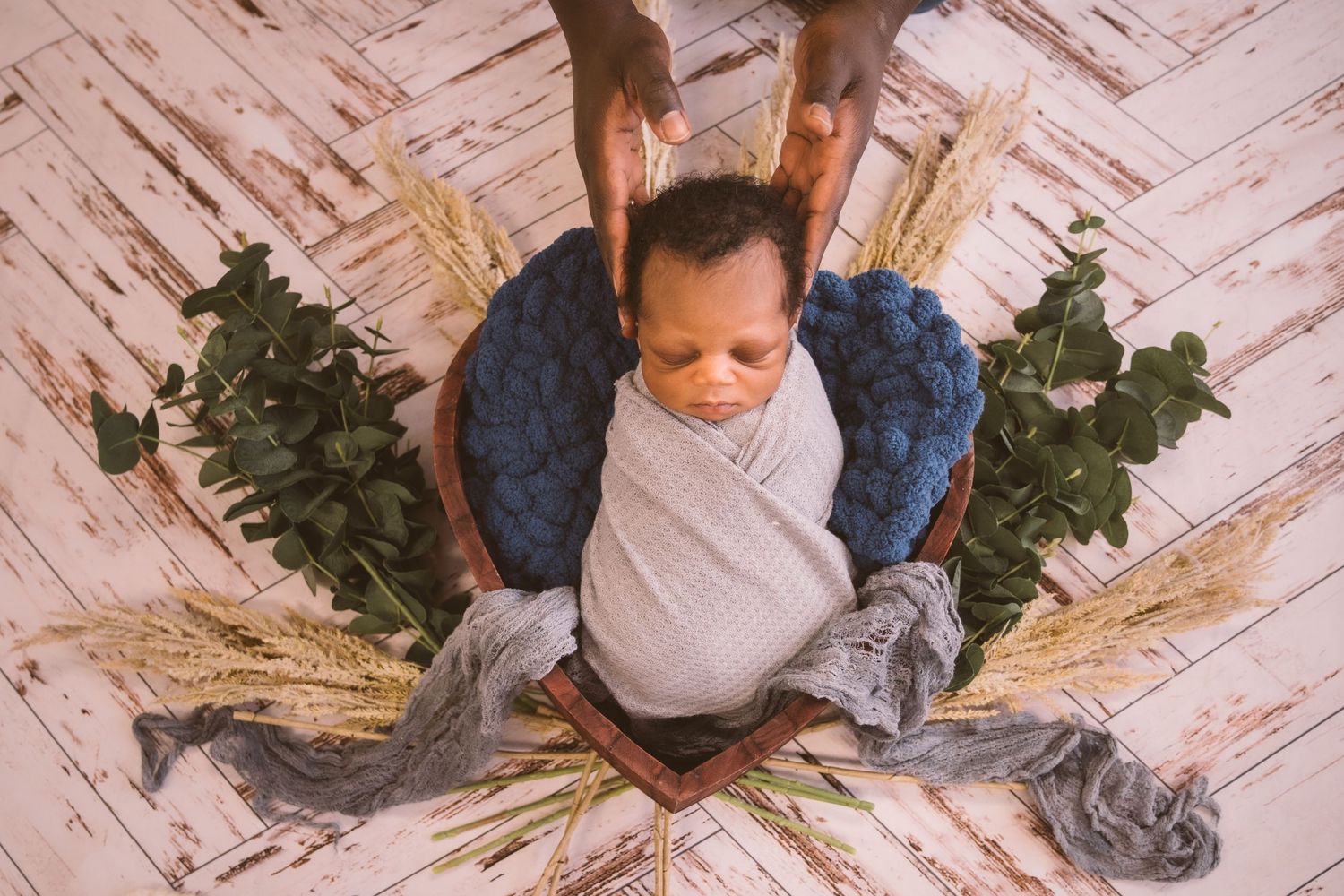 Overhead view of baby in gray wrap surrounded by greenery on herringbone floor.