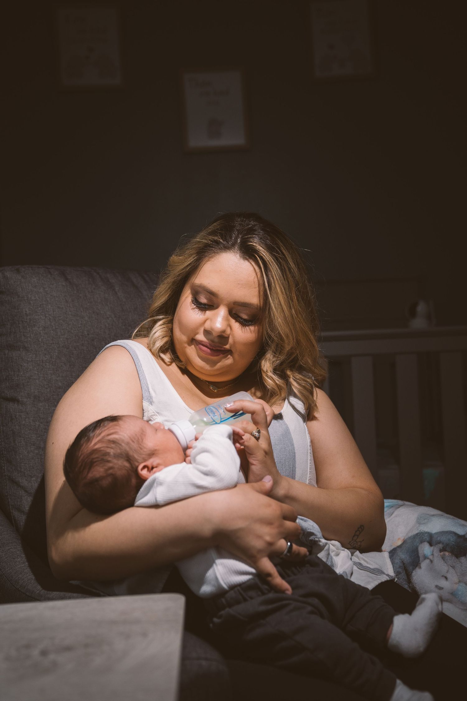 Tender moment between parent and baby in dim lighting on a couch.