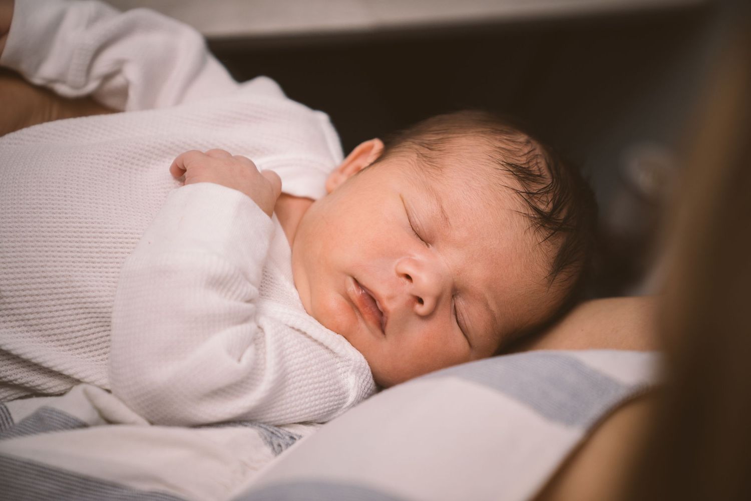 A sleeping infant wearing white clothing rests peacefully on soft bedding.