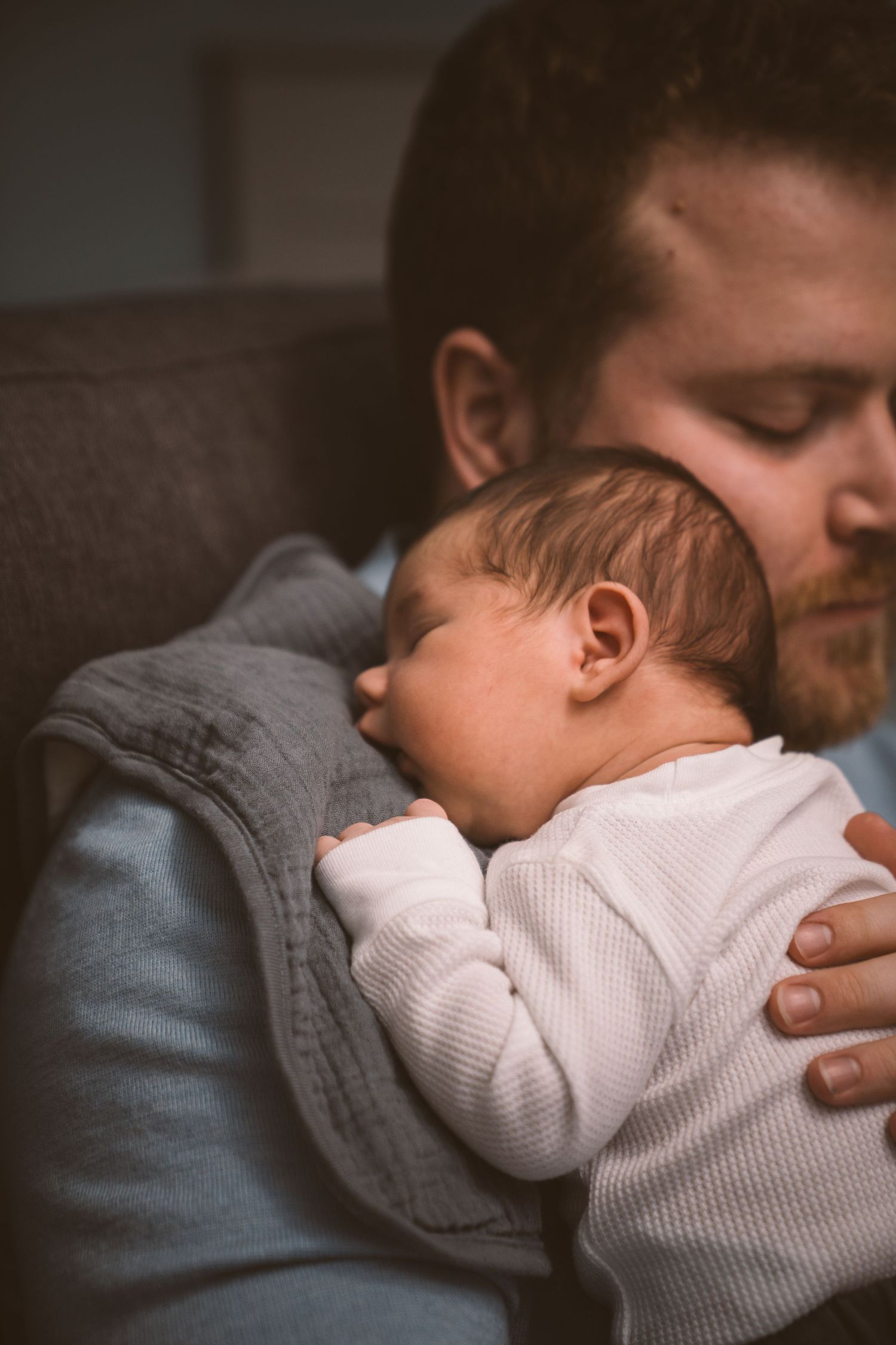 Baby in white onesie sleeping peacefully on parent's chest.
