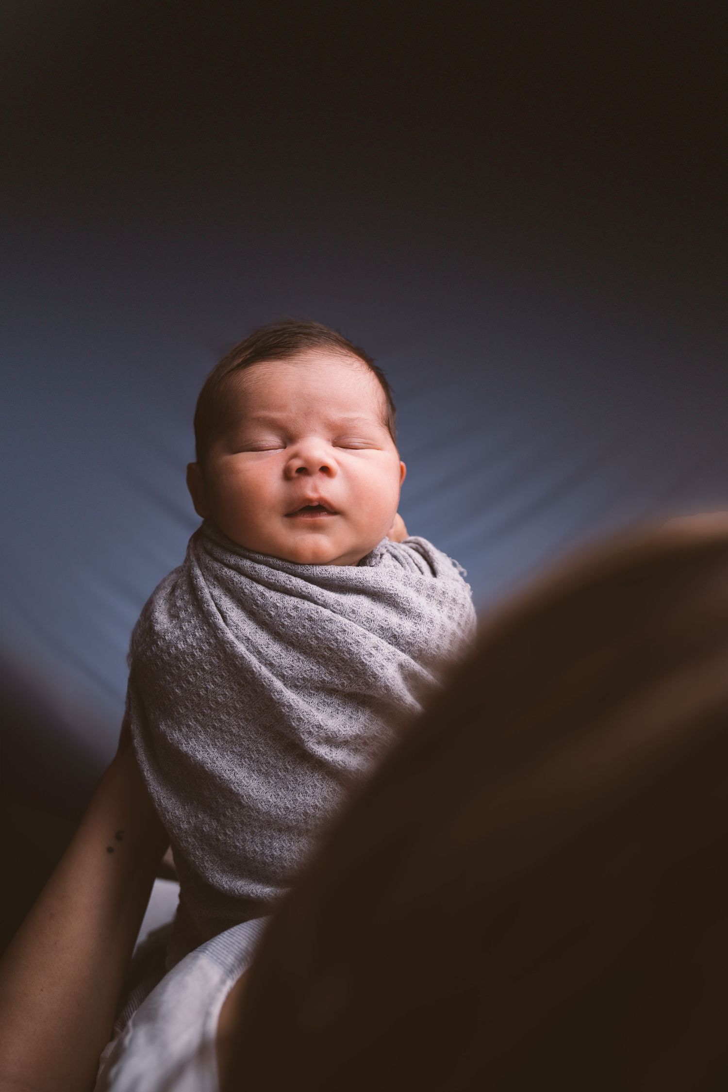 Newborn baby wrapped in soft gray blanket shown in progressive unwrapping sequence.