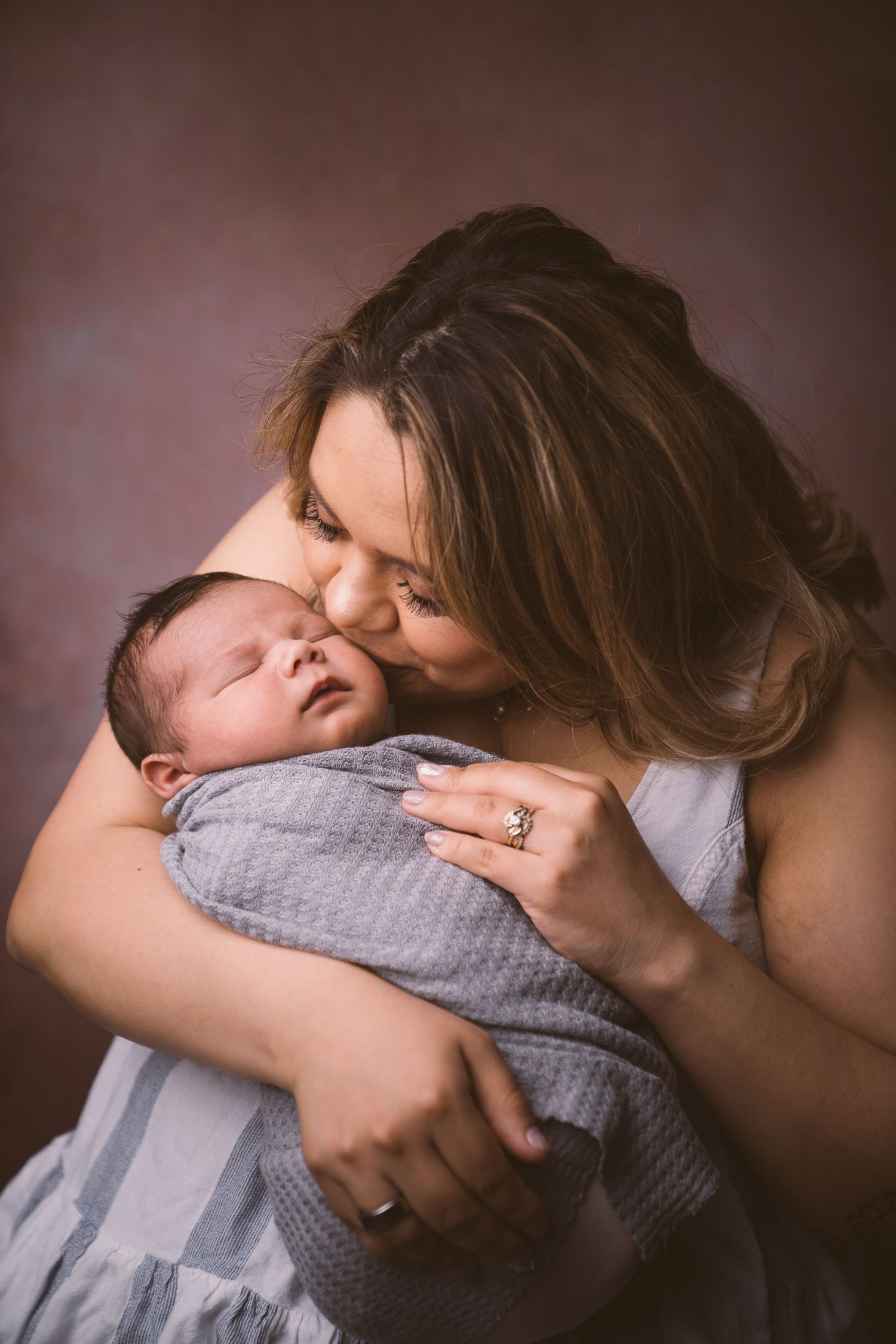 Emotional newborn photography session with warm brown backdrop.
