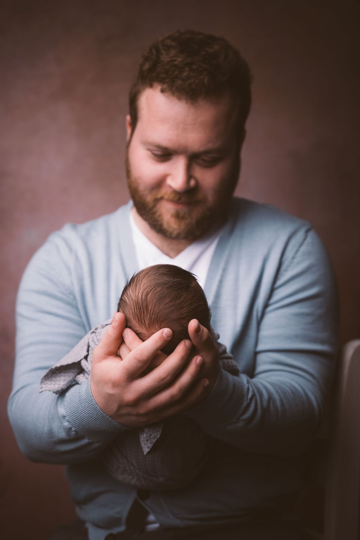 Person in light blue sweater tenderly holding and gazing at newborn baby.