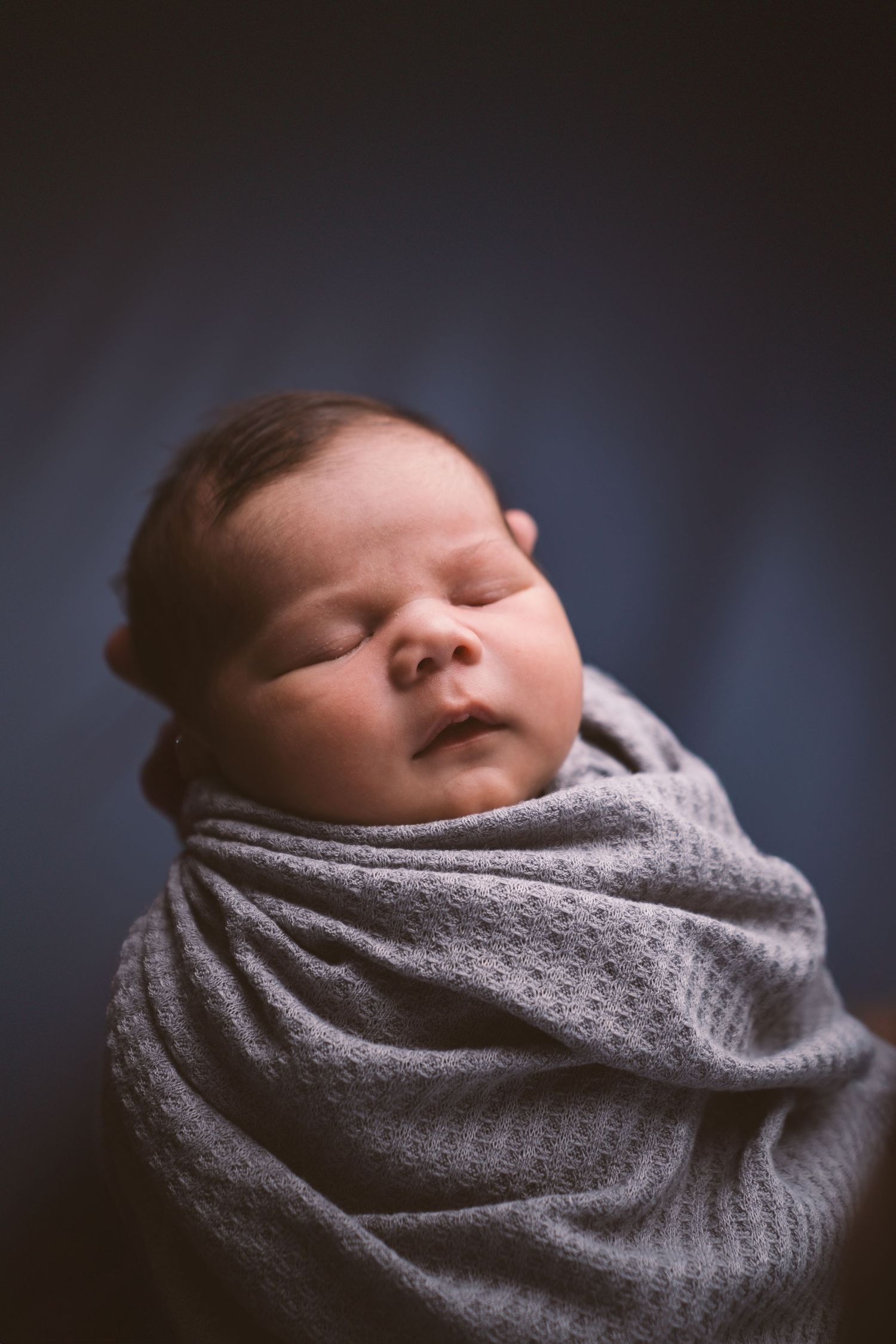 Close-up profile of a sleeping newborn wrapped in a soft gray blanket.