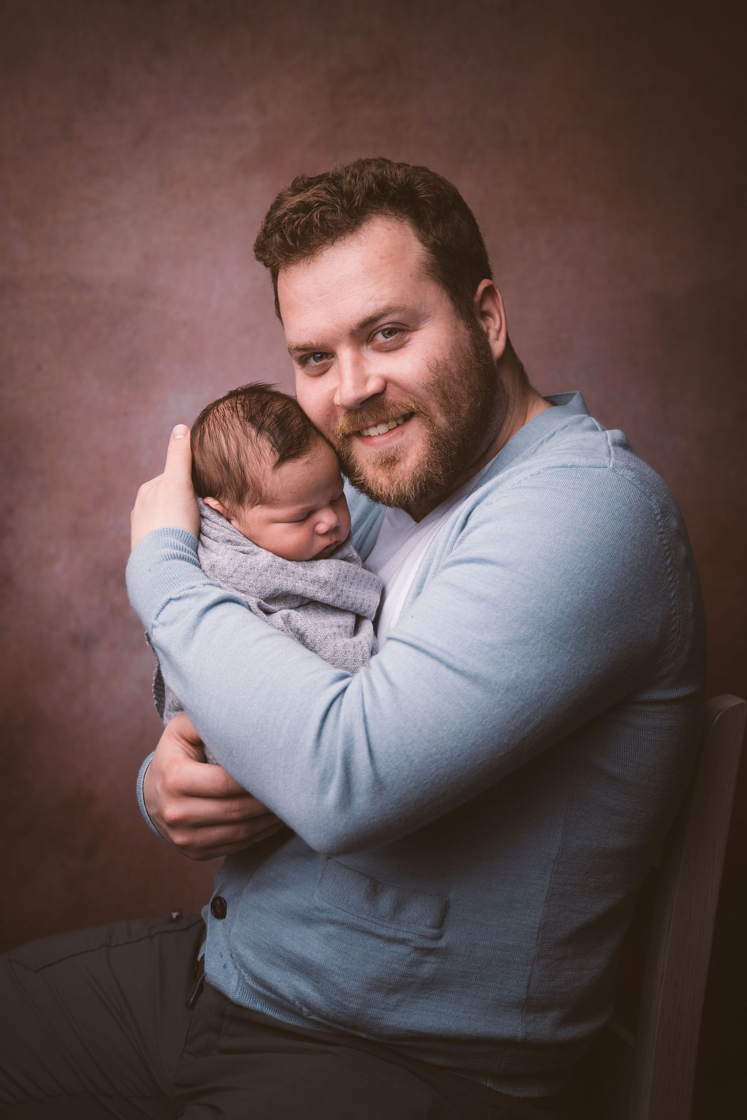Person in light blue sweater holding sleeping newborn in various gentle poses.