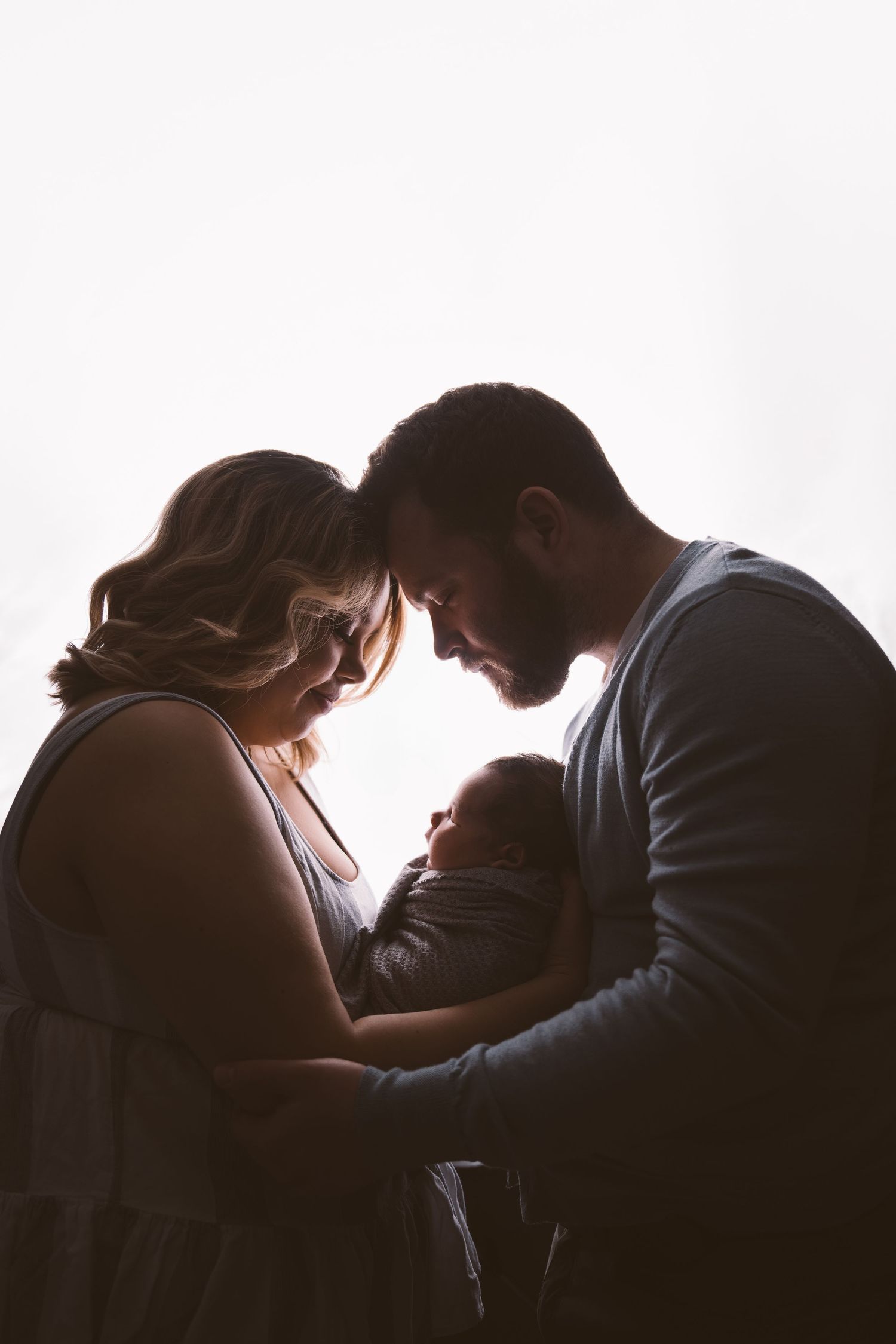 Silhouetted family sharing tender moment with newborn in dramatic lighting.