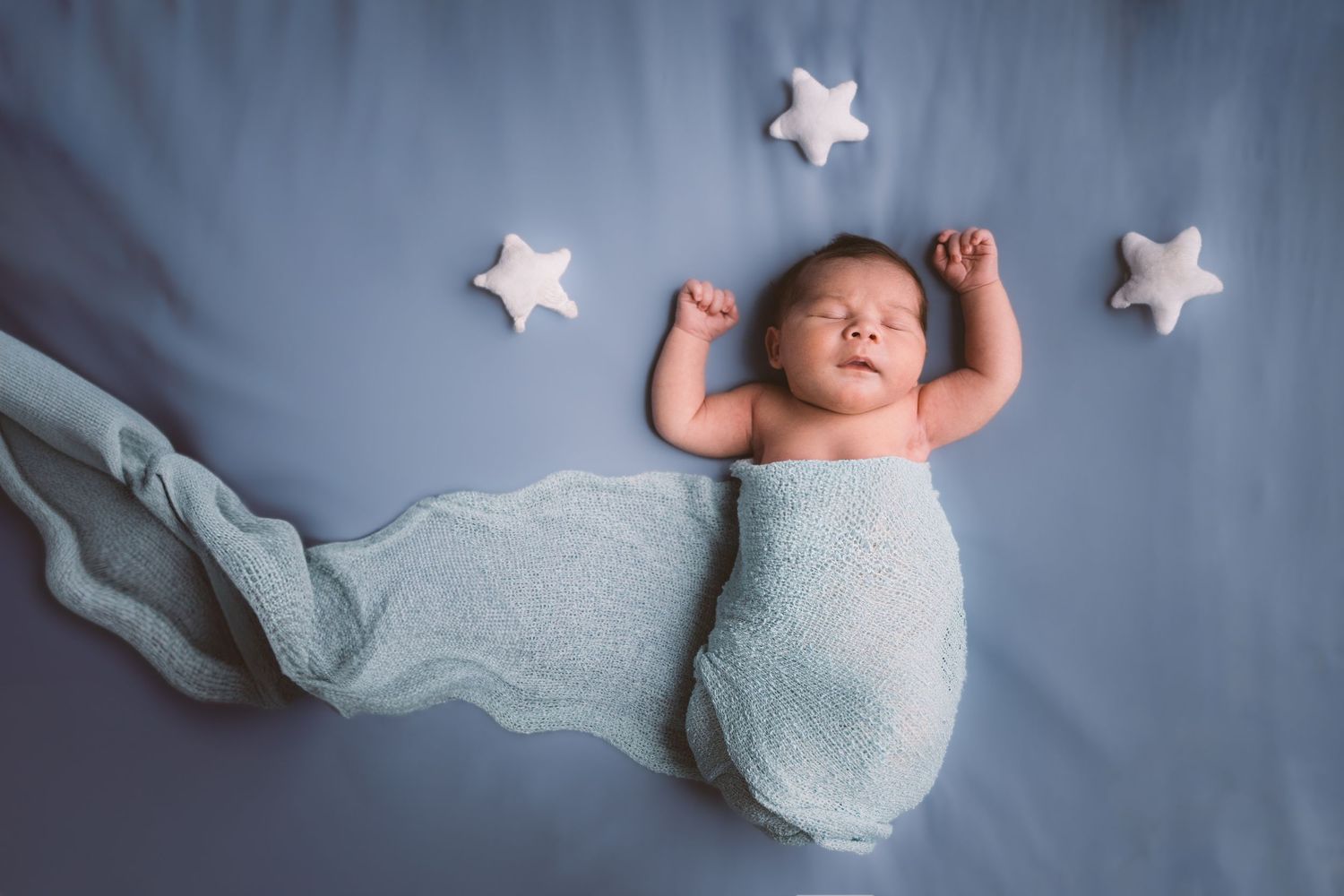 Sleeping newborn on blue backdrop with white star decorations.